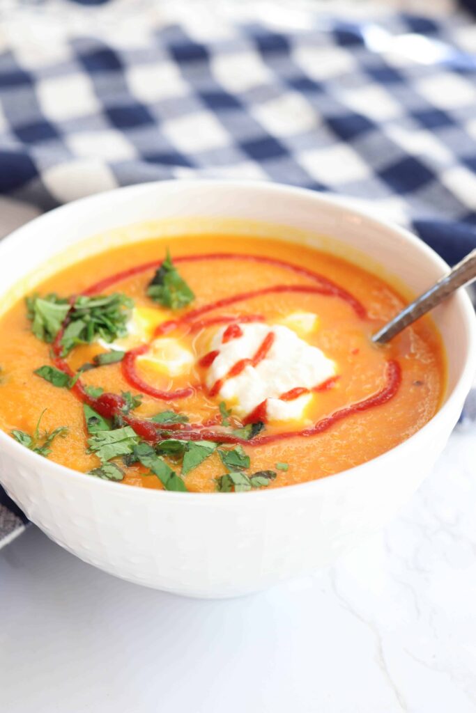 a white bowl with creamy carrot soup with Greek yogurt, Sriracha swirl and cilantro