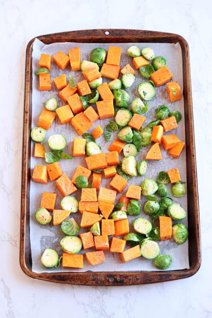 uncooked chopped up butternut squash and Brussels sprouts on a baking sheet