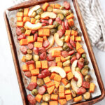 a baking sheet with cut up sausage, apples and vegetables