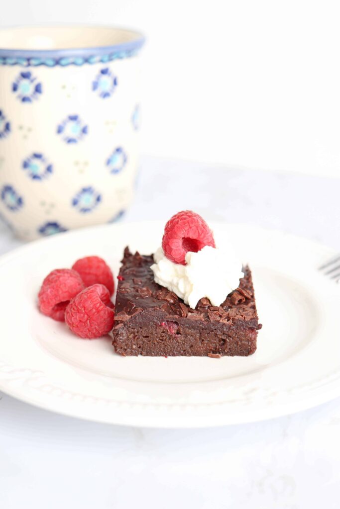 a piece of brownie with whipped cream and raspberries