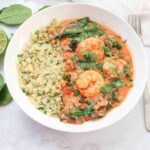 a white bowl of shrimp in tomato coconut sauce with spinach and cilantro with cauliflower rice