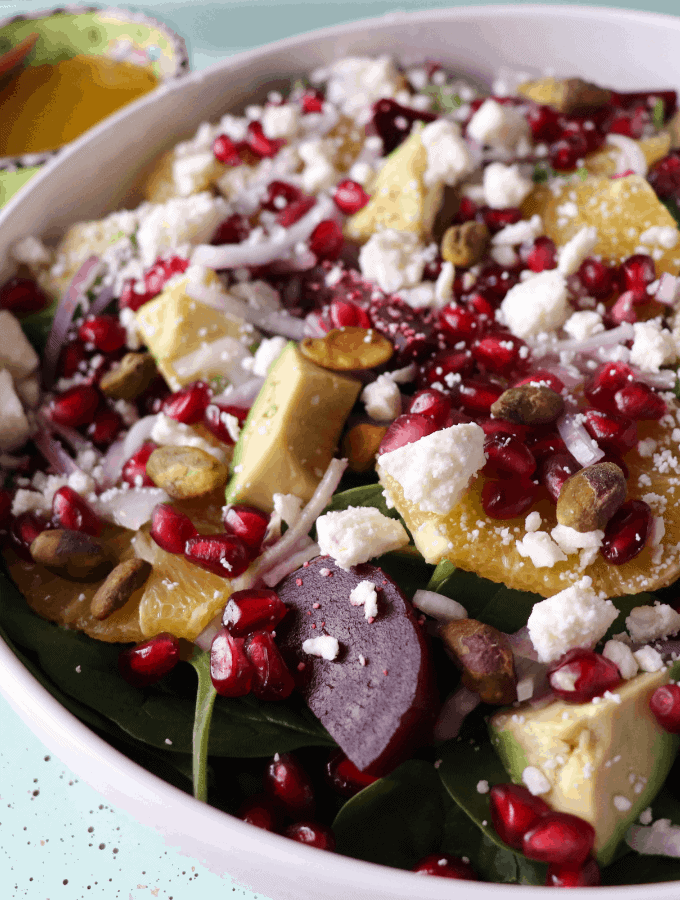 a bowl of salad with avocado, beets, orange, feta, pomegranate and red onions