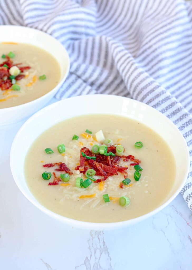 2 bowls of creamy potato cauliflower soup with bacon bits, grated cheese and scallions