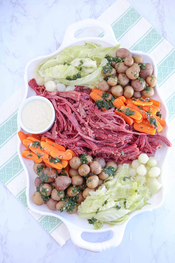 a tray with corned beef, carrots, cabbage, pearl onions, baby potatoes on marble countertop