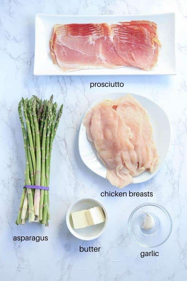 prosciutto, chicken, butter, garlic and asparagus on white plates on white marble surface