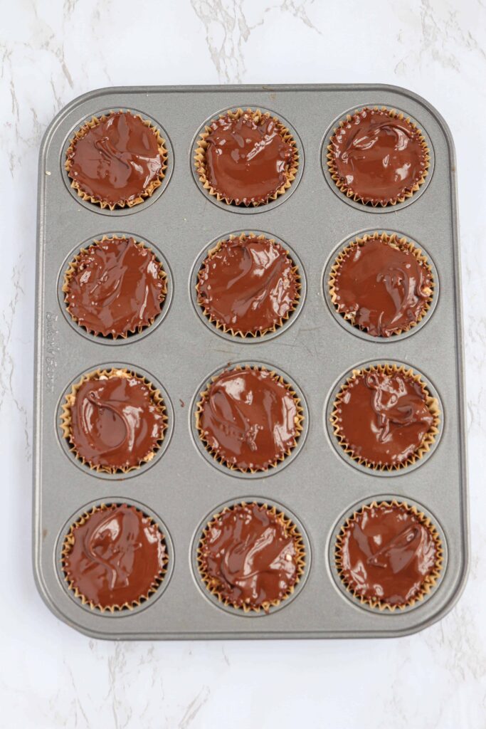 chocolate almond butter rice cups with chocolate in a mini muffin tin on white marble surface