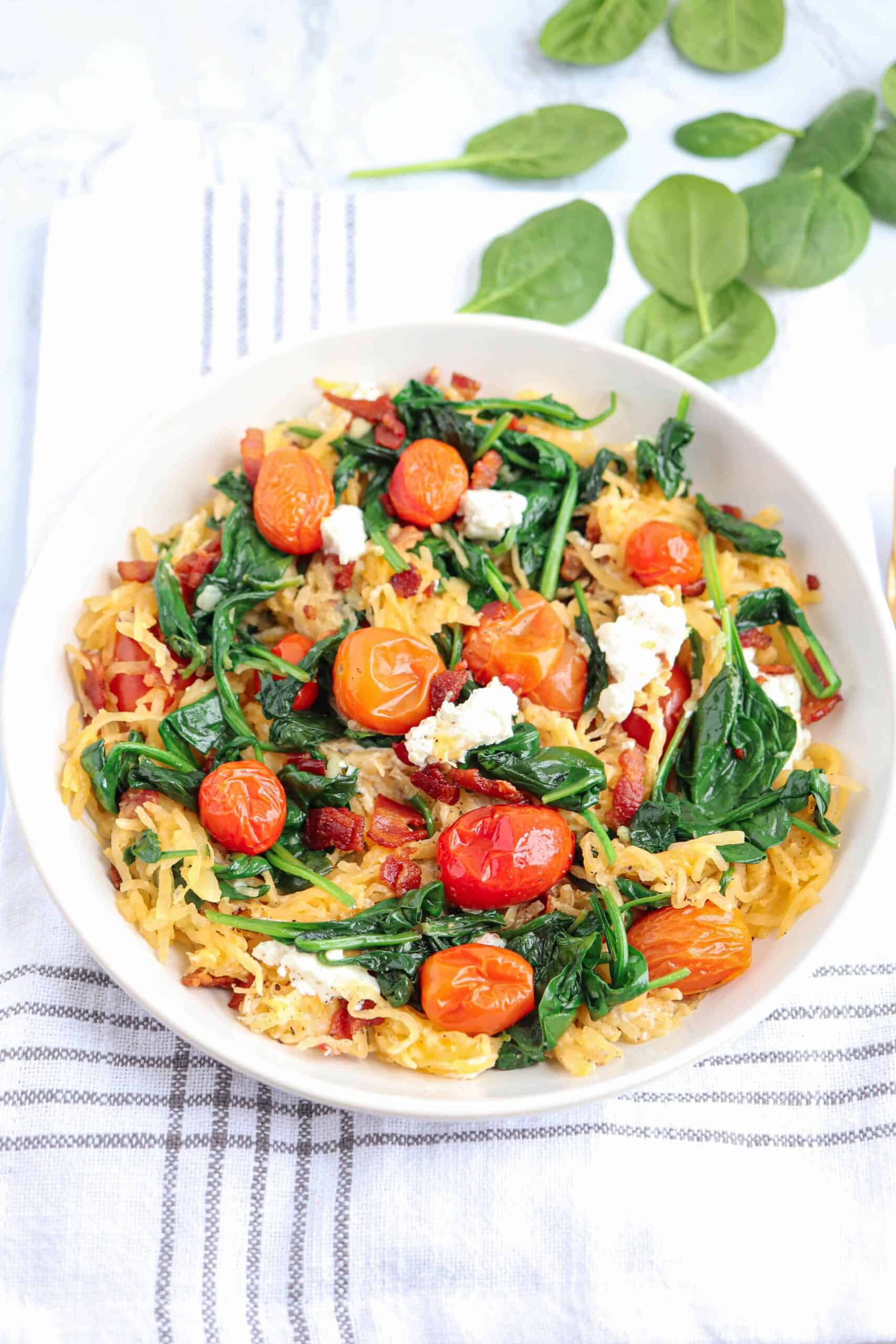 a white bowl of spaghetti squash with bacon, spinach, goat cheese 
