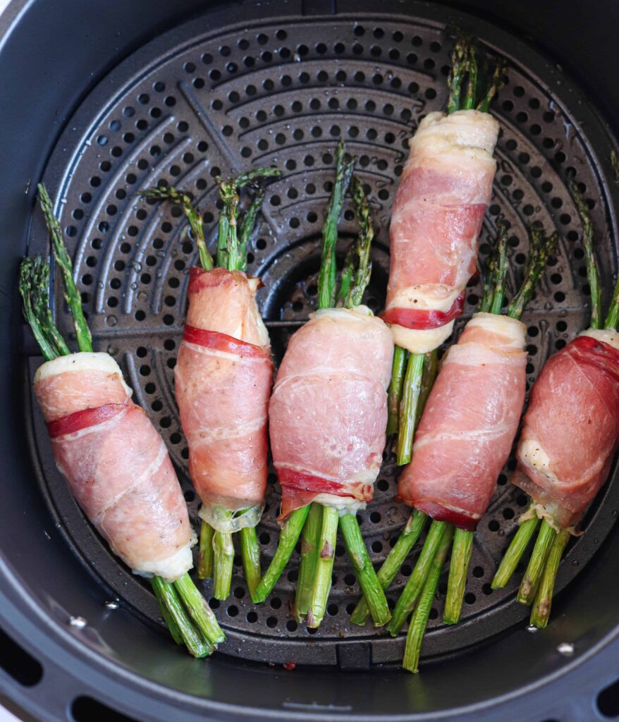 asparagus stuffed chicken wrapped in prosciutto in a black air fryer basket baked.