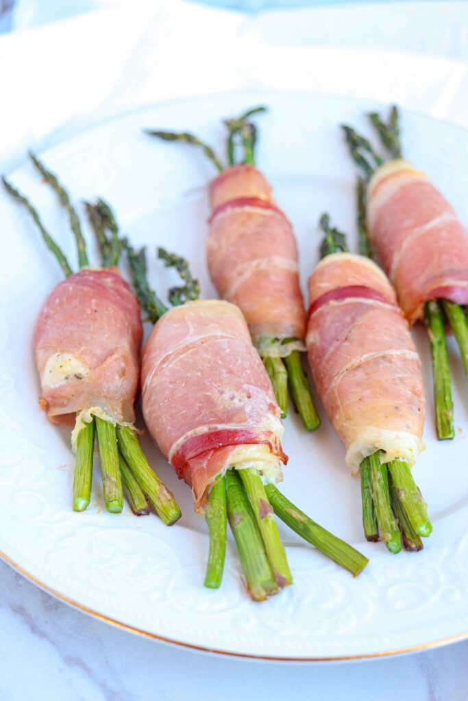 5 prosciutto wrapped asparagus stuffed chicken on a white plate.