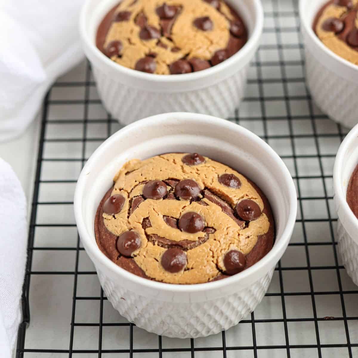 four white ramekins with chocolate peanut butter baked oats on a black cooling rack