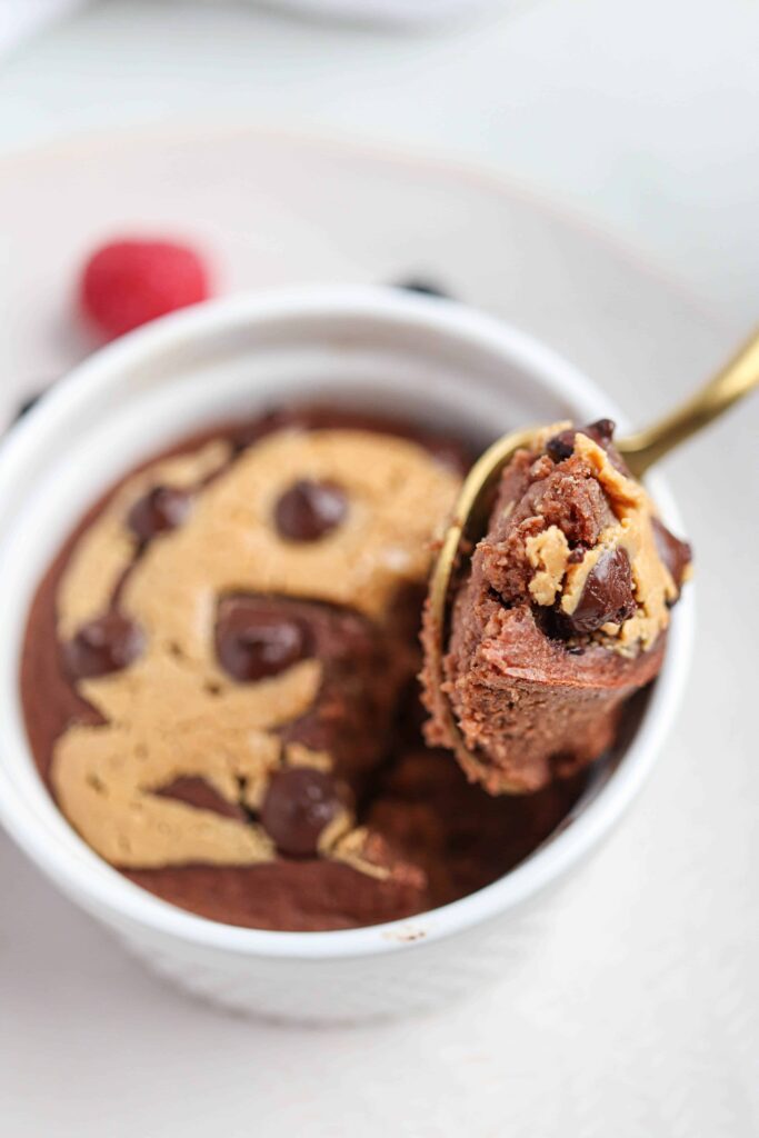one white ramekin with chocolate peanut butter baked oats with a gold spoon taken out with one bite taken out