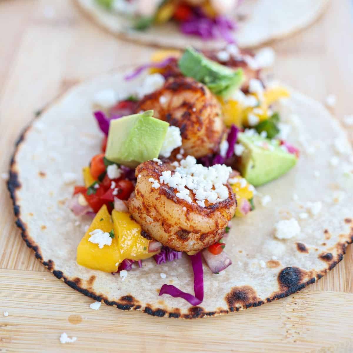 corn tortilla topped with shrimp, mango salsa, avocado, cotija cheese and cilantro on a wooden board