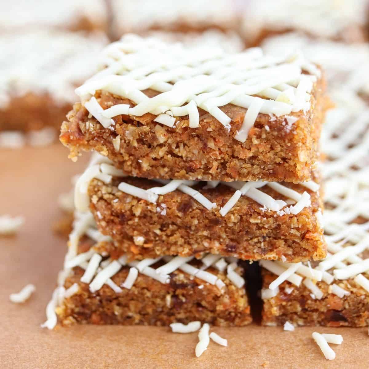 a stack of no-bake carrot cake bars with white chocolate drizzle
