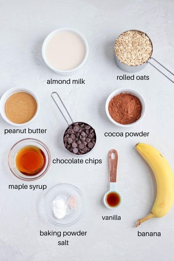 almond milk, cocoa powder, banana, vanilla, maple syrup, peanut butter, rolled oats, baking powder and salt laid out on light gray counter with captions underneath