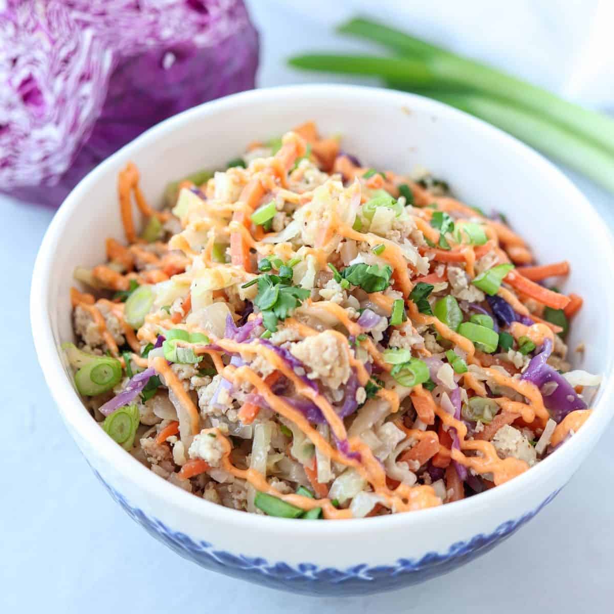 a white and blue bowl with egg roll in a bowl dish drizzled with sriracha mayo