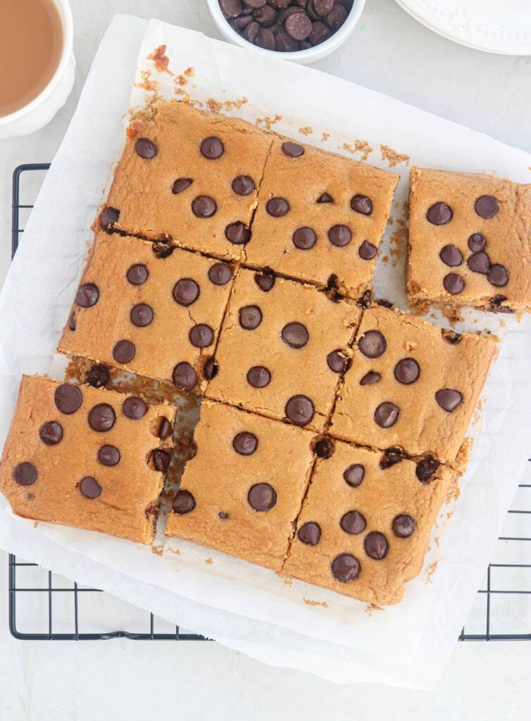 chickpea blondies with chocolate chips on white parchment paper on a black cooling rack.