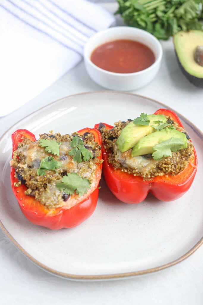 mexican quinoa stuffed red peppers with avocado and fresh cilantro on a plate.