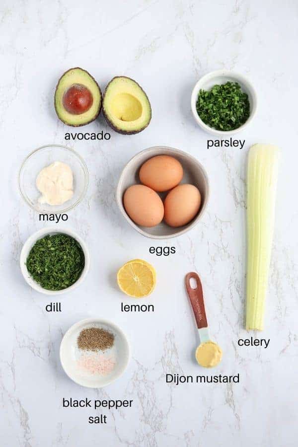 egg avocado salad ingredients laid out on white marble surface with text labels