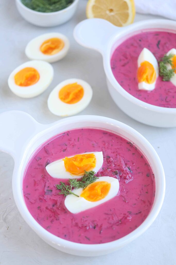 Polish cold beet soup in a white bowl with 2 quarters of boiled ehh on top.