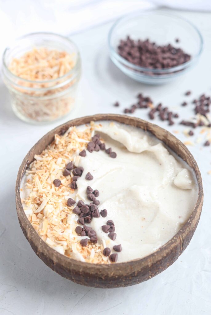 vanilla coconut smoothie with chocolate chips and toasted coconut in a coconut shell bowl 