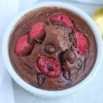 A chocolate protein baked oats dish served in a white ramekin, topped with fresh raspberries and chocolate chips.