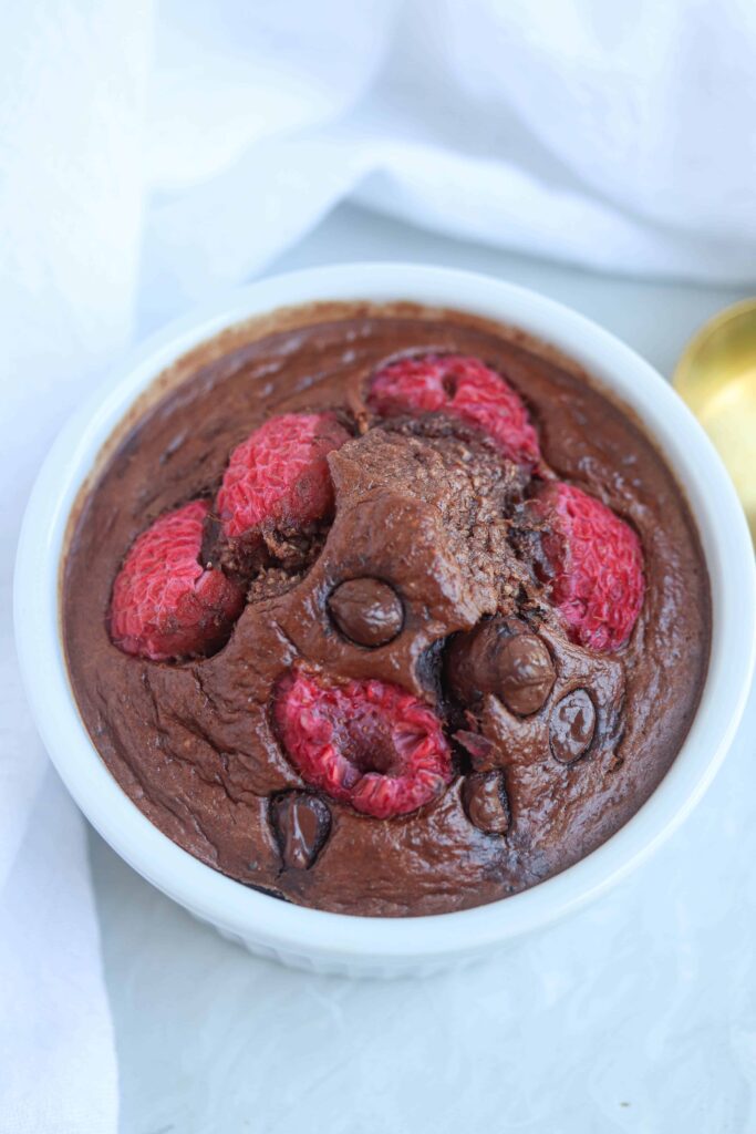 chocolate protein baked oats with chocolate chips and raspberries in a white ramekin