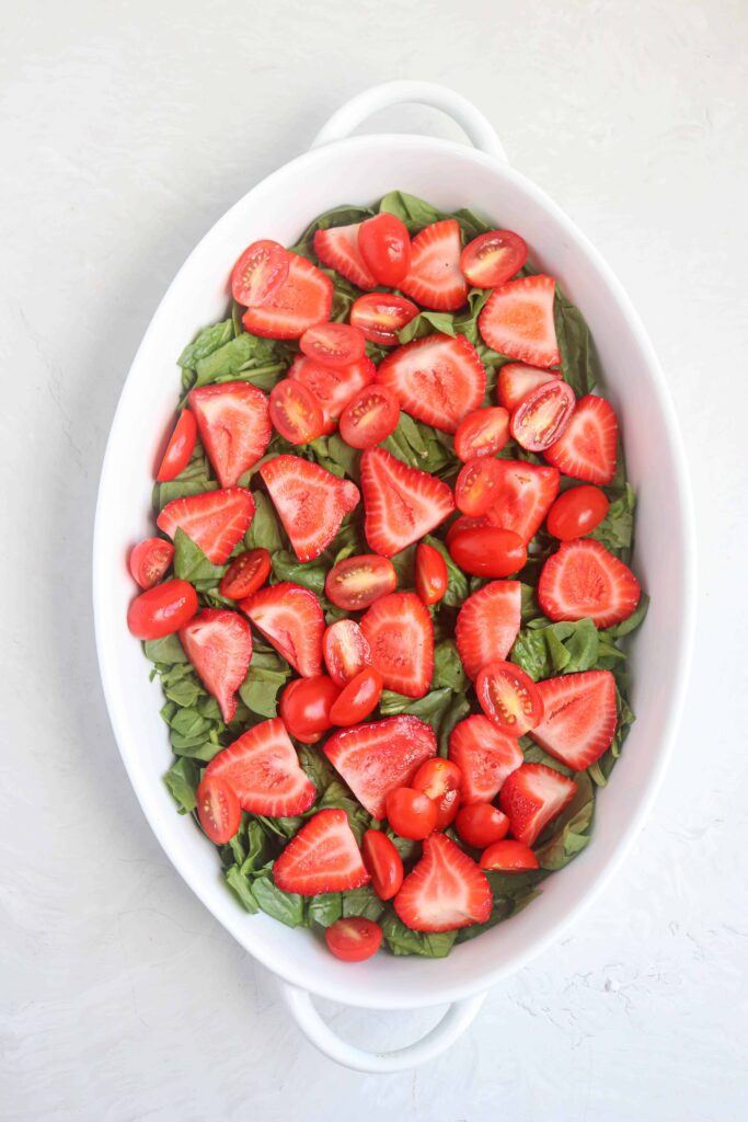 an oval dish with chopped baby spinach, strawberries and cherry tomatoes