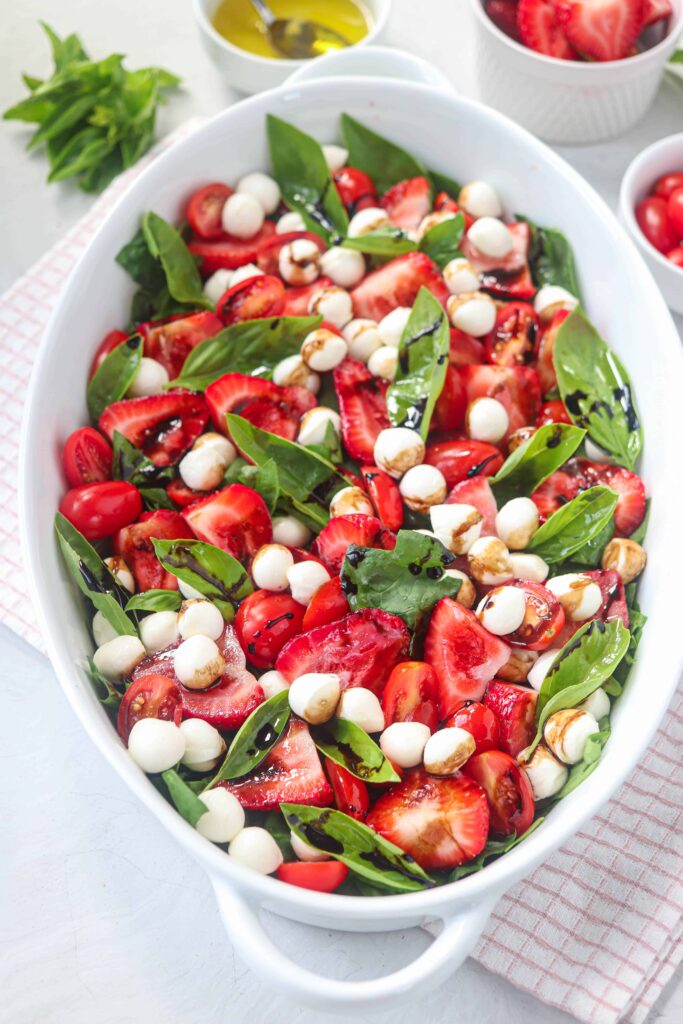 strawberry spinach caprese salad served in an oval casserole dish on light gray surface on a red a white kitchen towel