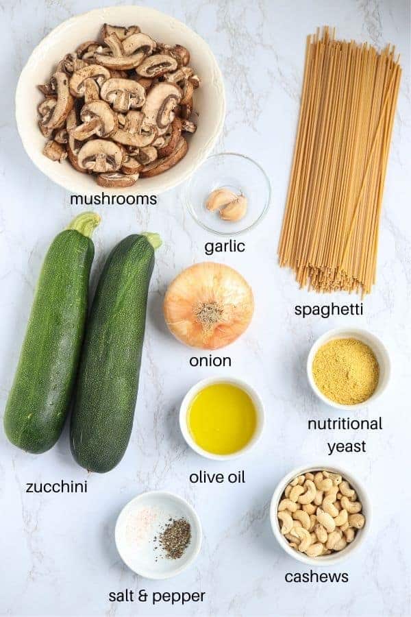 mushroom zucchini spaghetti ingredients laid out on a white marble surface with labels
