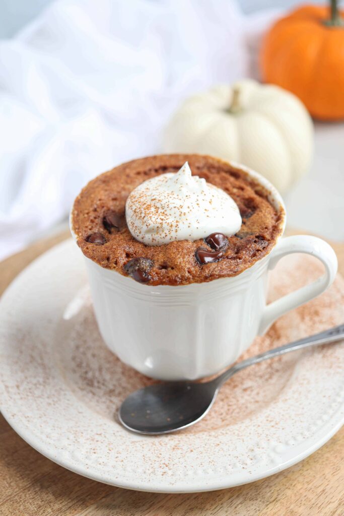 pumpkin mug cake with a dollop of whipped cream and cinnamon in a white teacup on a saucer