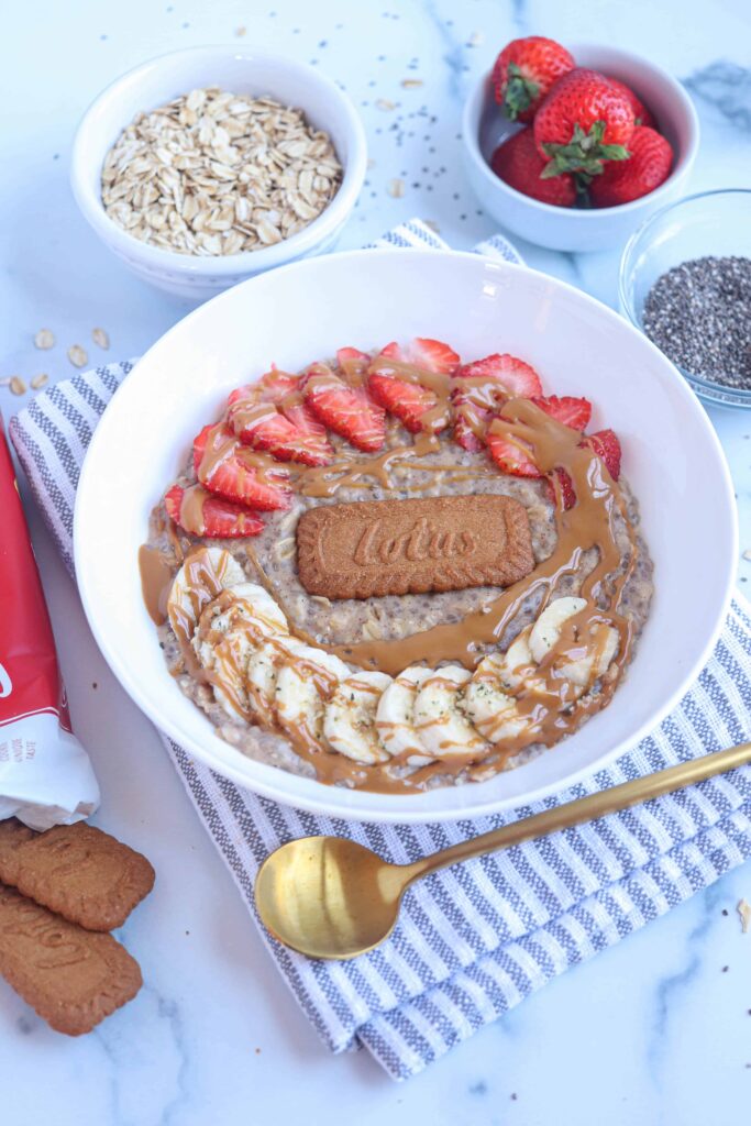 Biscoff oatmeal in a white bowl with strawberries, bananas, one Biscoff cookie and a drizzle of Biscoff cookie spread on top