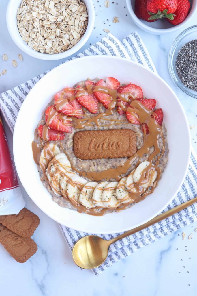 Biscoff oatmeal in a white bowl with strawberries, bananas, one Biscoff cookie and a drizzle of Biscoff cookie spread on top
