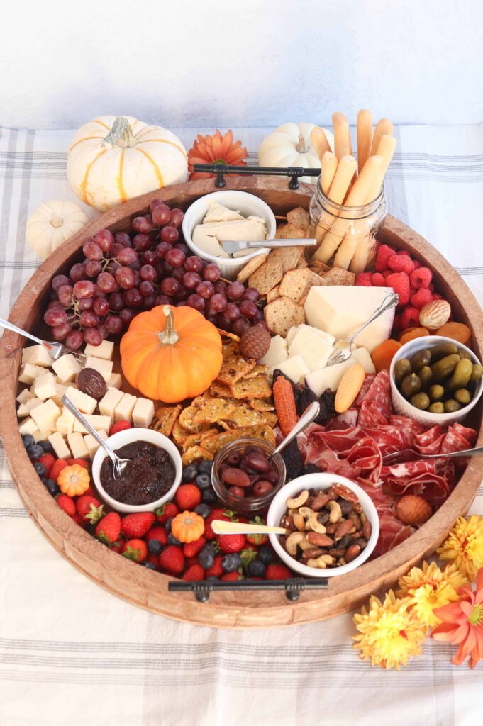 large round fall charcuterie board with cheese, fruit, cured meats, nuts and condiments. 