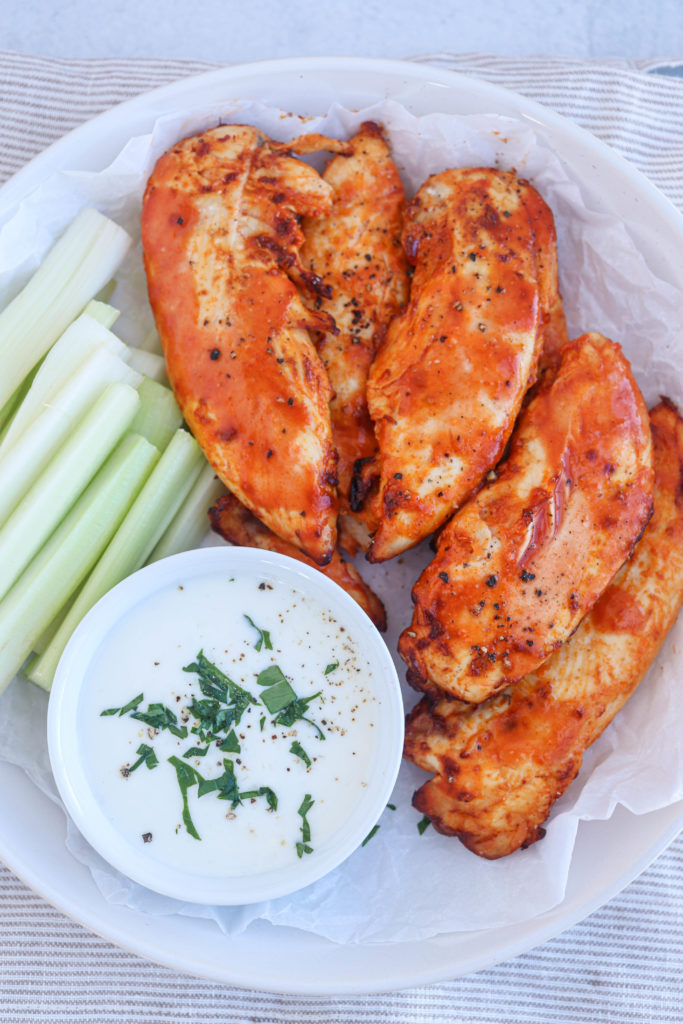air fryer buffalo chicken tenders on a white round place with a side of celery and blue cheese dressing, close up