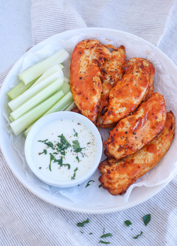 air fryer buffalo chicken tenders on a white round place with a side of celery and blue cheese dressing
