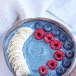 blue smoothie bowl topped with blueberries, raspberries and sliced bananas