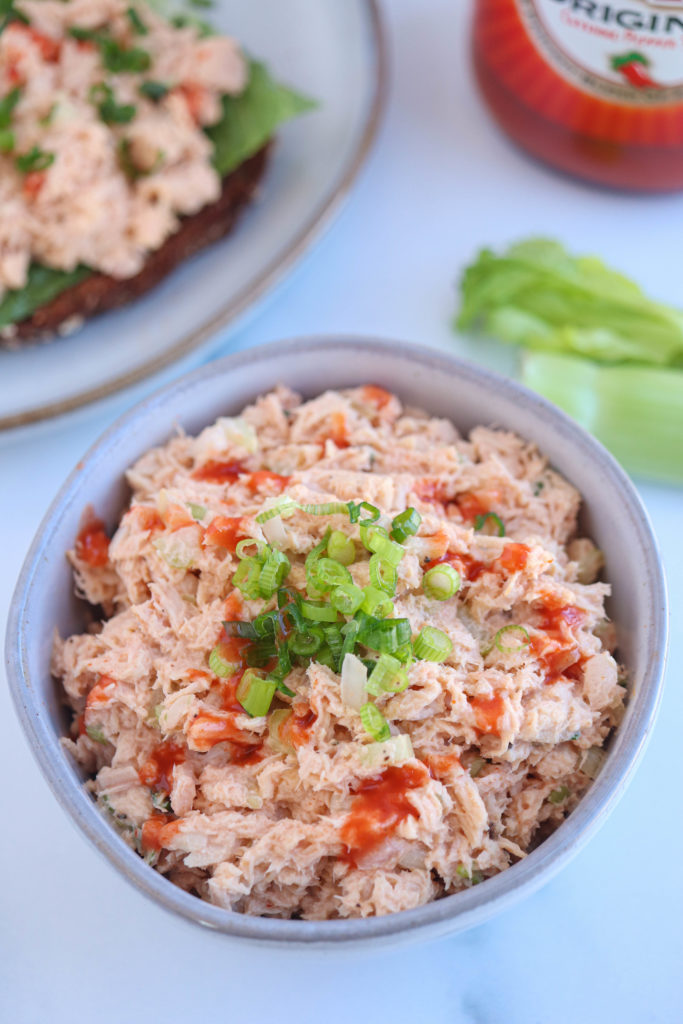 buffalo tuna salad drizzled with hot sauce and sprinkled with chives in a small gray bowl.