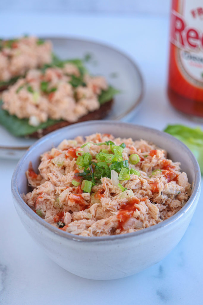 buffalo tuna salad drizzled with hot sauce and sprinkled with chives in a small gray bowl.