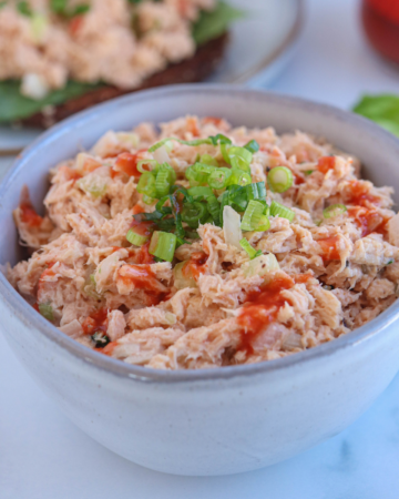 buffalo tuna salad in a small gray bowl drizzled with hot sauce and sprinkled with chives