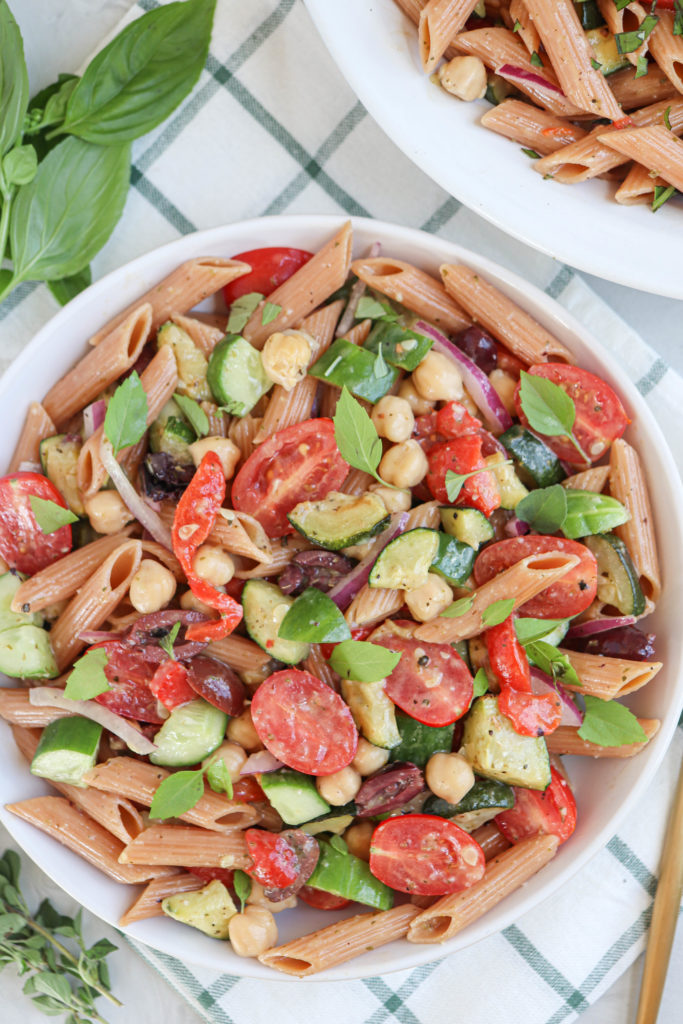 lentil pasta salad with tomatoes, cucumbers, chickpeas and herbs in a white bowl