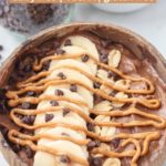 snickers smoothie bowl in a coconut bowl topped with banana slices, peanuts, chocolate chips and a peanut butter drizzle