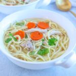 a white bowl with homemade chicken noodle soup with carrots and parsley leaves