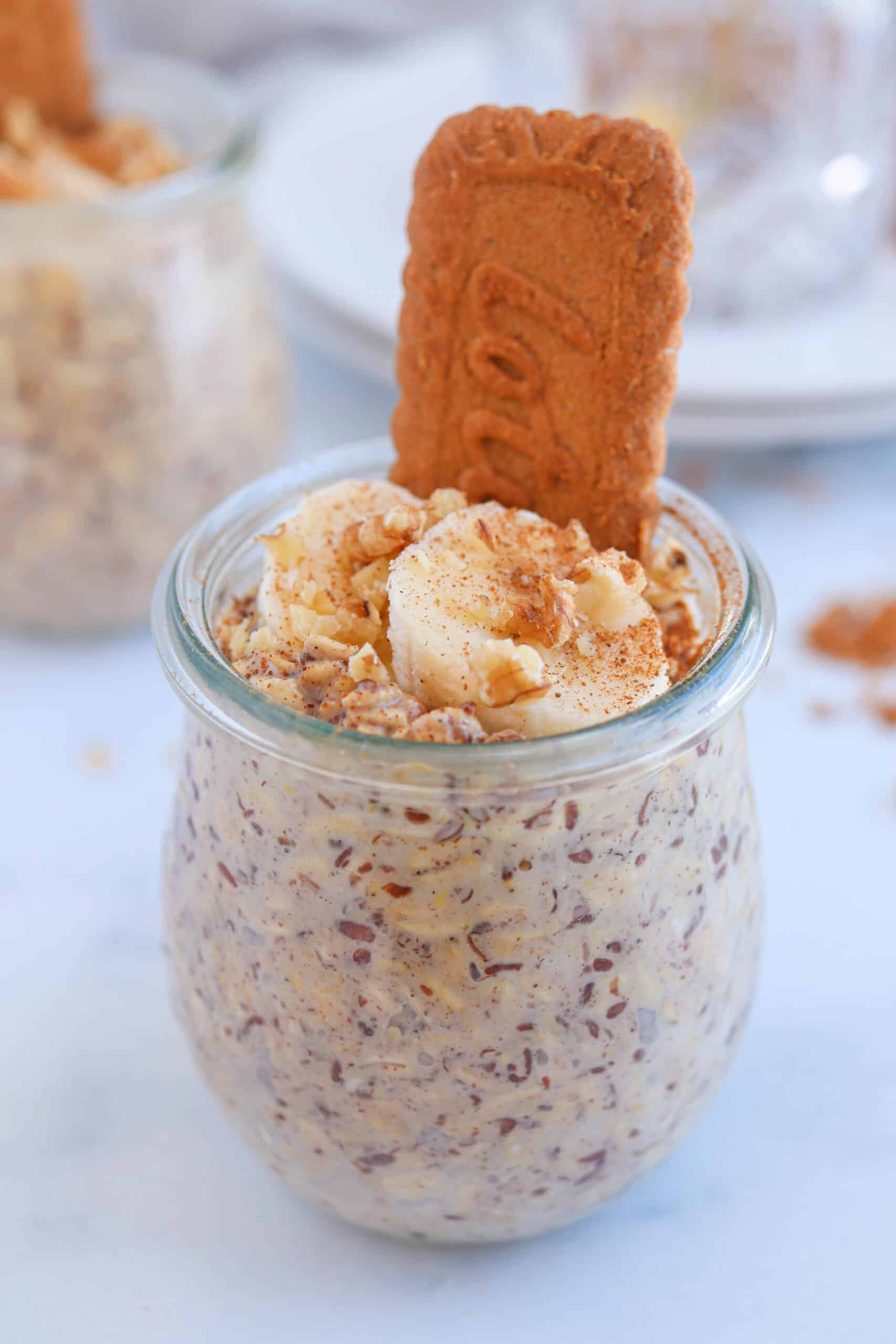 biscoff overnight oats in a tulip jar topped with sliced banana, walnuts and crushed biscoff cookies.