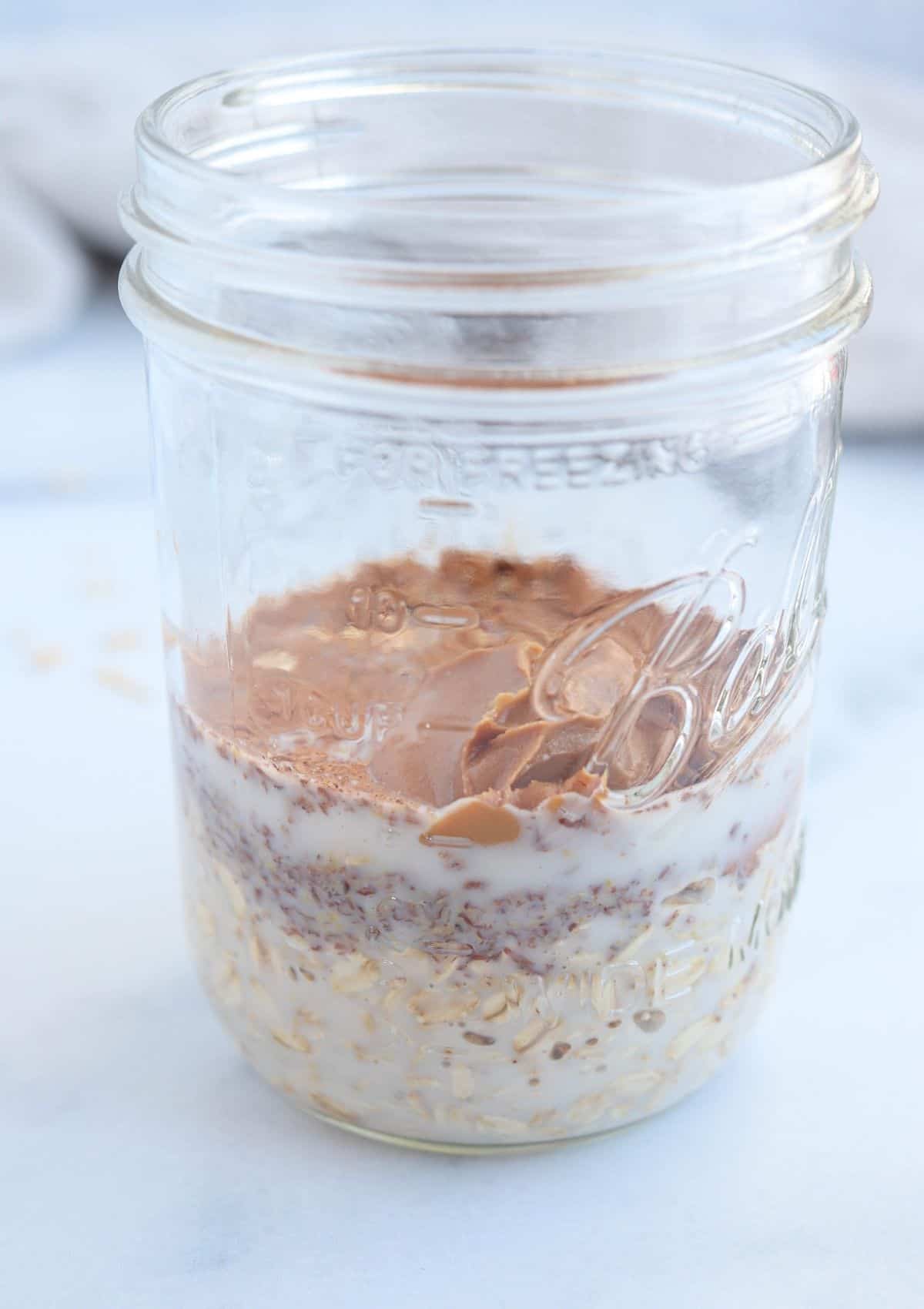 mason jar with oats, flaxseed, biscoff spread and plant milk.