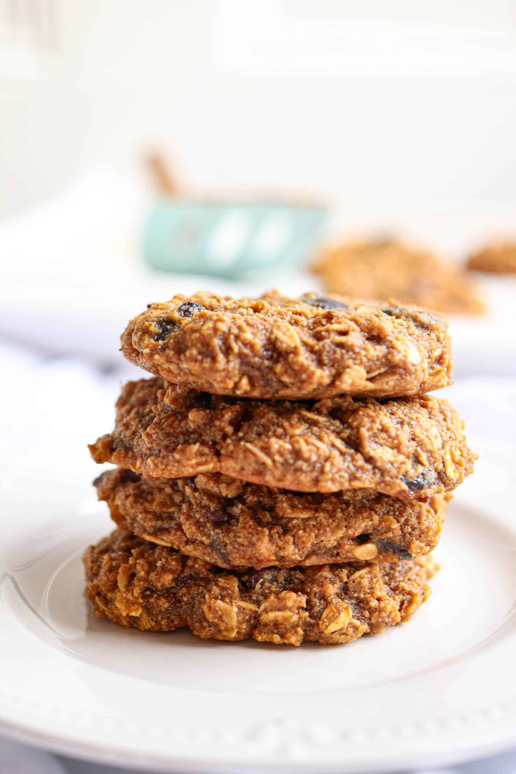A stack of five homemade, rustic oatmeal cookiesโperfect for healthy banana breakfast recipesโsits on a white plate with visible oats and raisins and a soft, bright background.
