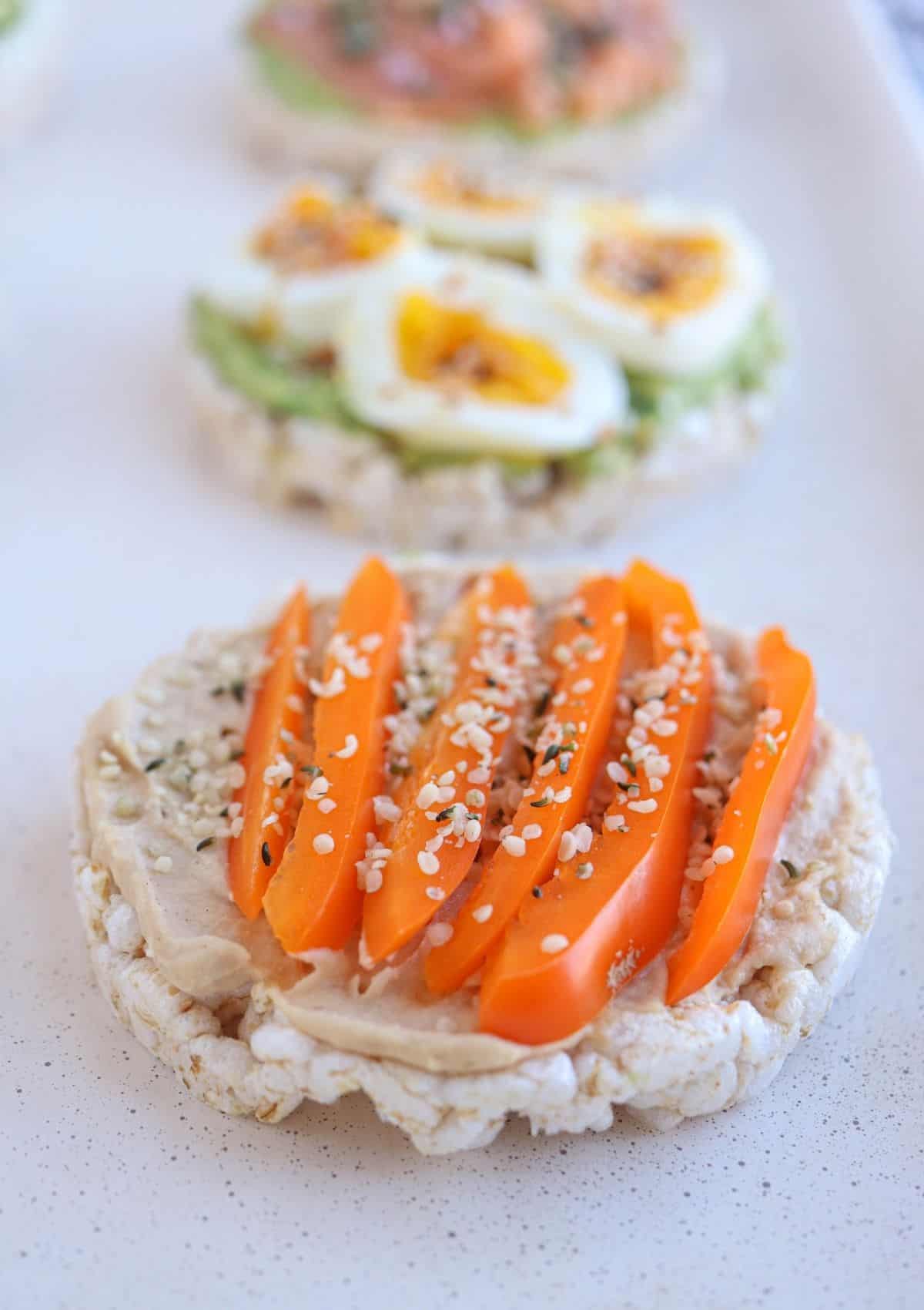 rice cake topped with hummus and sliced orange bell pepper and hemp hearts.