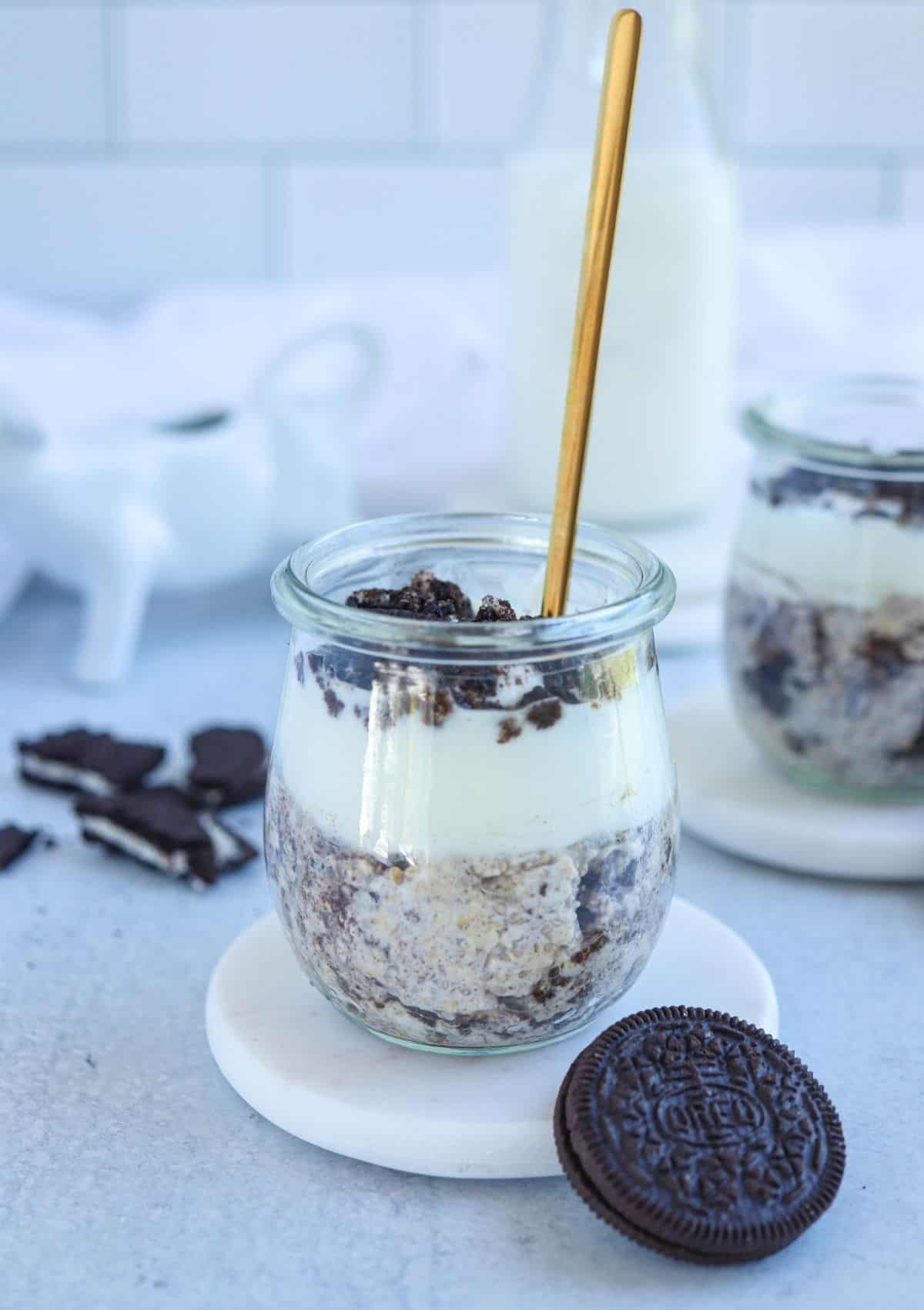 oreo overnight oats topped with yogurt and crushed oreos in a small glass jar with a golden spoon.