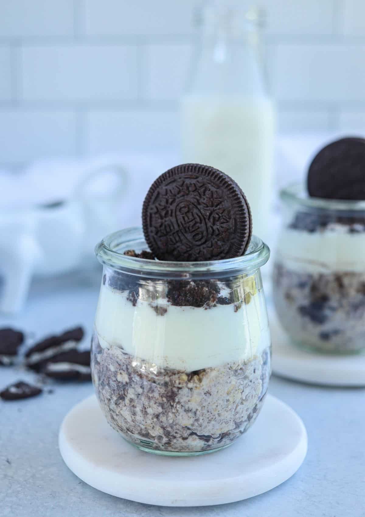 oreo overnight oats topped with yogurt and crushed oreos in a small glass jar decorated with a whole Oreo cookie.