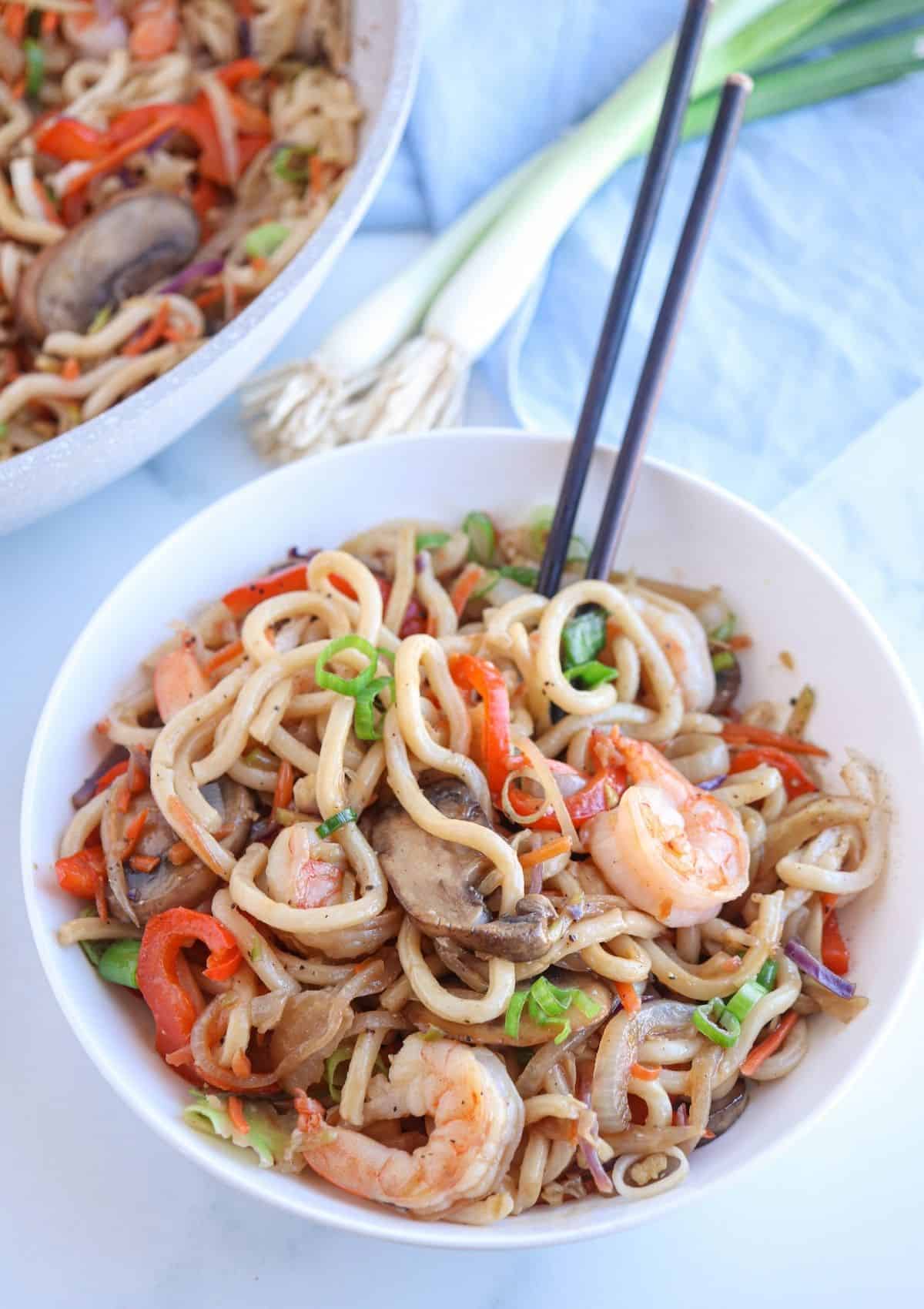 a white bowl of shrimp yaki udon noodle stir-fry with mushrooms and veggies. 