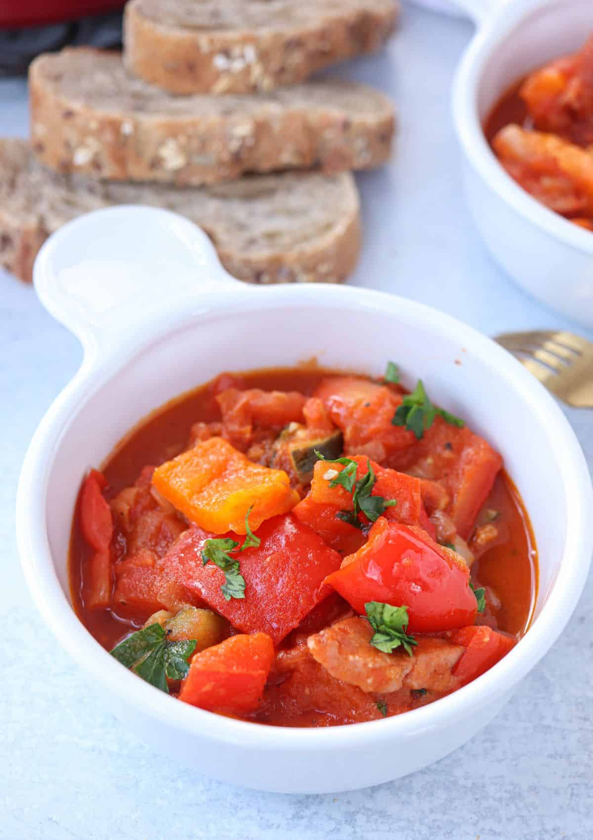 tomato pepper stew with sausage and zucchini in a white bowl with a side of crusty bread.